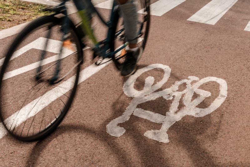 Ciclista pedalando em uma ciclovia sinalizada com símbolo de bicicleta no asfalto.