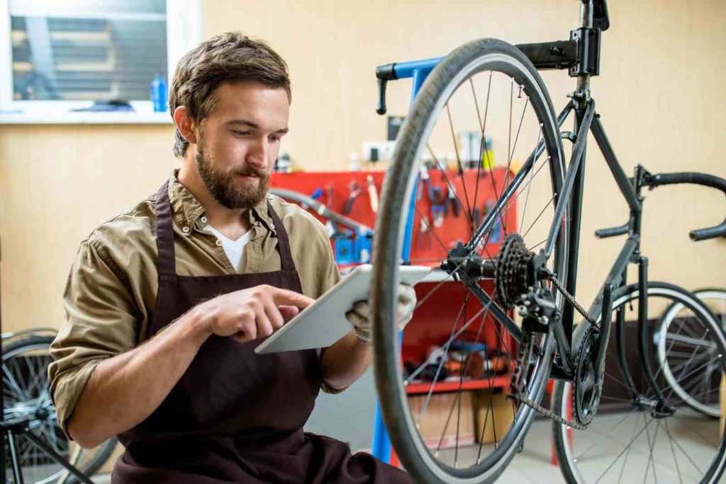 Mecânico analisando uma bicicleta em manutenção com auxílio de um tablet na oficina.