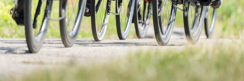 Grupo de ciclistas pedalando em uma estrada, com destaque para as rodas das bicicletas em movimento.