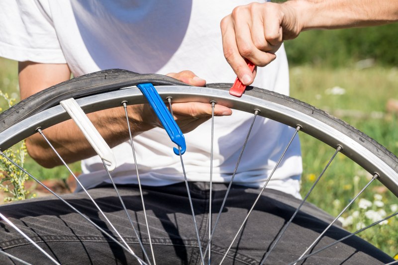 Pessoa removendo o pneu da roda de uma bicicleta com espátulas durante a manutenção.